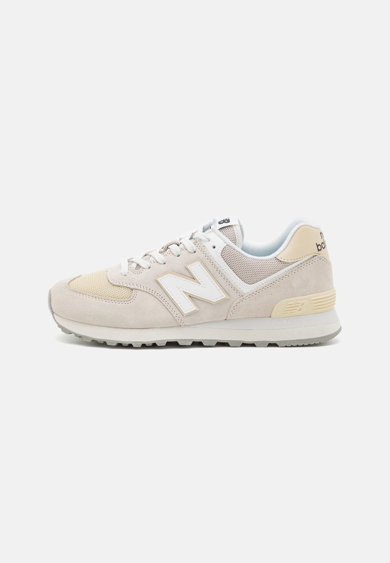 Light beige sneakers with a suede and mesh upper, featuring a white “N” logo, lace closure, and a rubber sole. Subtle yellow accents.