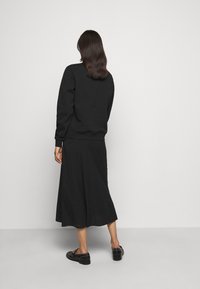 Svart sweatshirt med långa ärmar kombinerad med en svart, flödande midikjol och svarta skor med nitar. Minimalistisk design med en elegant siluett.