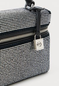 Borsa strutturata nera decorata con borchie argentate, dotata di chiusura con zip superiore e un piccolo dettaglio a lucchetto argentato. Manico in pelle liscia.