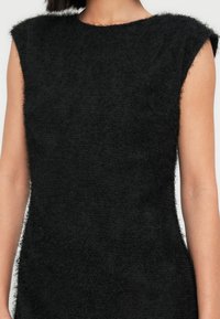 Μαύρο αμάνικο τοπ με υφή και μαλακό, χνουδωτό τελείωμα. Διαθέτει ψηλό λαιμό και απλή, κομψή σιλουέτα.