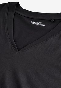 T-shirt noir en coton col V avec une étiquette intérieure visible indiquant "NEXT" et les informations de taille.