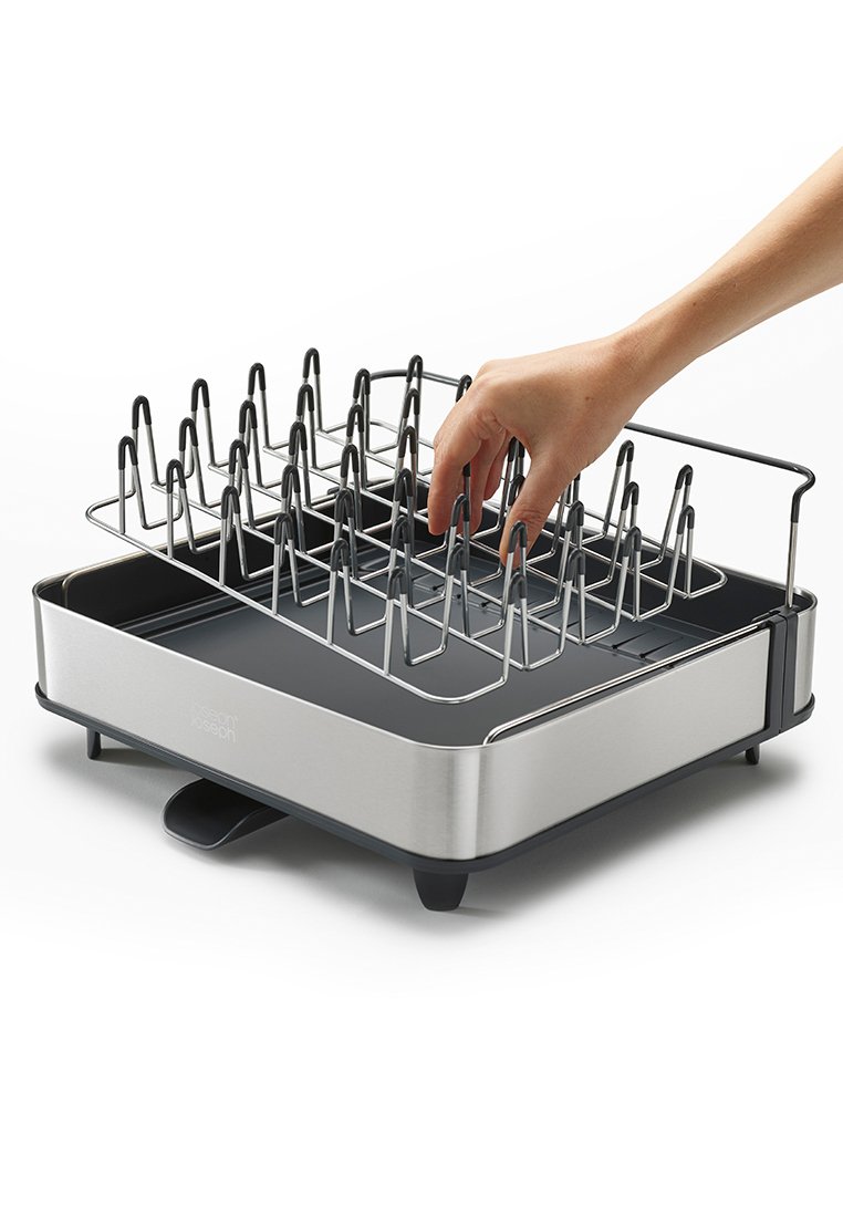 Edelstahlregal mit mehreren vertikalen Stangen, einem schwarzen Sockel und einem Tablett zum Kochen oder Abtropfen. Eine Hand greift nach dem Regal.