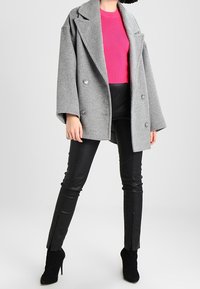 Šedý oversized kabát z vlněné směsi s dvojřadovým zapínáním, doplněný jasně růžovým žebrovaným svetrem a černými koženými kalhotami se štěrbinami.