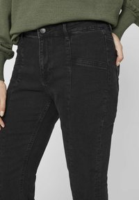 Melna denima bikses ar augstu jostu, vieglu stiepli un gludu tekstūru. Ar redzamu aizmugures kabatas šuvi. 