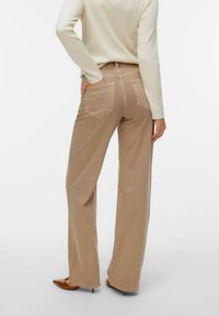 Beżowe spodnie o szerokich nogawkach wykonane z denimu, z tylnymi kieszeniami i średnim stanem. Tekstura jest gładka, o jasnym, neutralnym kolorze.