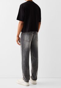 Svart t-shirt med kort ärm, matchad med urtvättade grå jeans och vita sneakers. Tyget verkar mjukt med en avslappnad passform och rak ben-design.