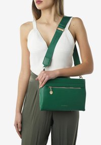 Grøn læder crossbody taske med en frontlomme med lynlås, justerbar rem og en glat tekstur. Har minimalistisk branding og hardware detaljer.