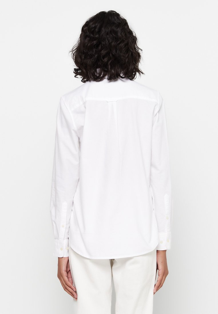 Weißes Baumwollhemd mit langen Ärmeln, Knopfmanschetten, Detail am Rücken und abgerundetem Saum. Glatte Textur, klassisches Design und taillierte Passform.