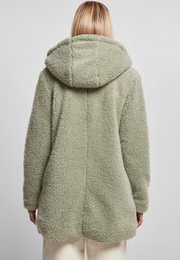Abrigo de forro polar en verde claro, con una gran capucha, superficie texturizada, mangas largas y un diseño de longitud media con un dobladillo redondeado.