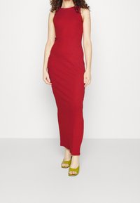 Rotes ärmelloses Maxikleid mit figurbetontem Schnitt, glatter Textur und knielangem Schlitz, kombiniert mit grünen offenen High Heels.