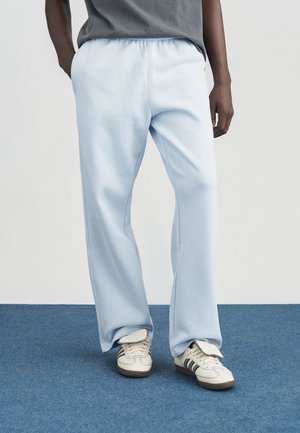 Pantalon de survêtement bleu clair avec taille élastique, poches et coupe décontractée, associé à des baskets blanches avec des accents bleu marine.