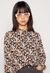 Blusa floral com fundo preto, apresentando flores em tons de rosa, branco e castanho. Inclui um colarinho com babados e fecho de botão.