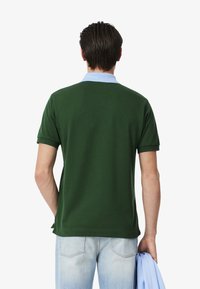 Grön pikétröja med ljusblå krage, korta ärmar och rak skärning, i kombination med ljusblå jeans. Slät textur och klassisk design.