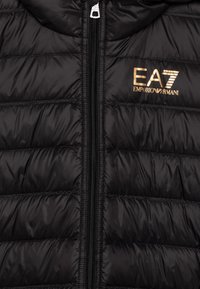 Schwarze gepolsterte Jacke mit Reißverschluss, ausgestattet mit einem gesteppten Design und einem goldenen EA7 Emporio Armani Logo auf der Brust.