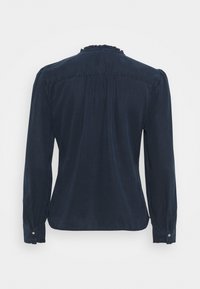 Blusa a maniche lunghe di colore blu navy con scollo a volant, schiena arricciata e polsini con bottoni; tessuto liscio con una leggera lucentezza.
