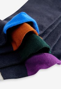 Quattro calze lavorate a maglia in blu, arancione, verde e viola, con risvolti a coste e una morbida texture su uno sfondo di tessuto scuro.