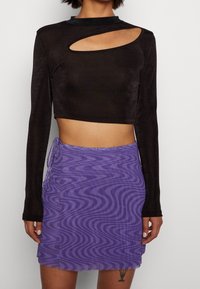 Svart långärmad croppad topp med utskärning på sidan; kombinerad med en lila minikjol med vågigt mönster och rynkade detaljer på sidan.