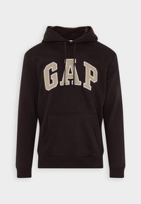 Felpa nera con cappuccio, tasca a marsupio frontale, cappuccio con cordino e logo "GAP" in tessuto beige sul petto. Materiale morbido e design casual.