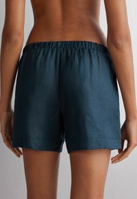 Mörkblå linshorts med resårmidja, med en rak fåll och minimal sömdetalj, sedd bakifrån.