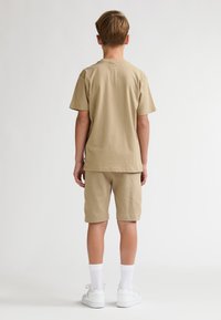 Kaki t-shirt med korte ærmer og matchende shorts i bomuldsmateriale. Har rund hals, løs pasform og sidelommer. Bruges med hvide sneakers.