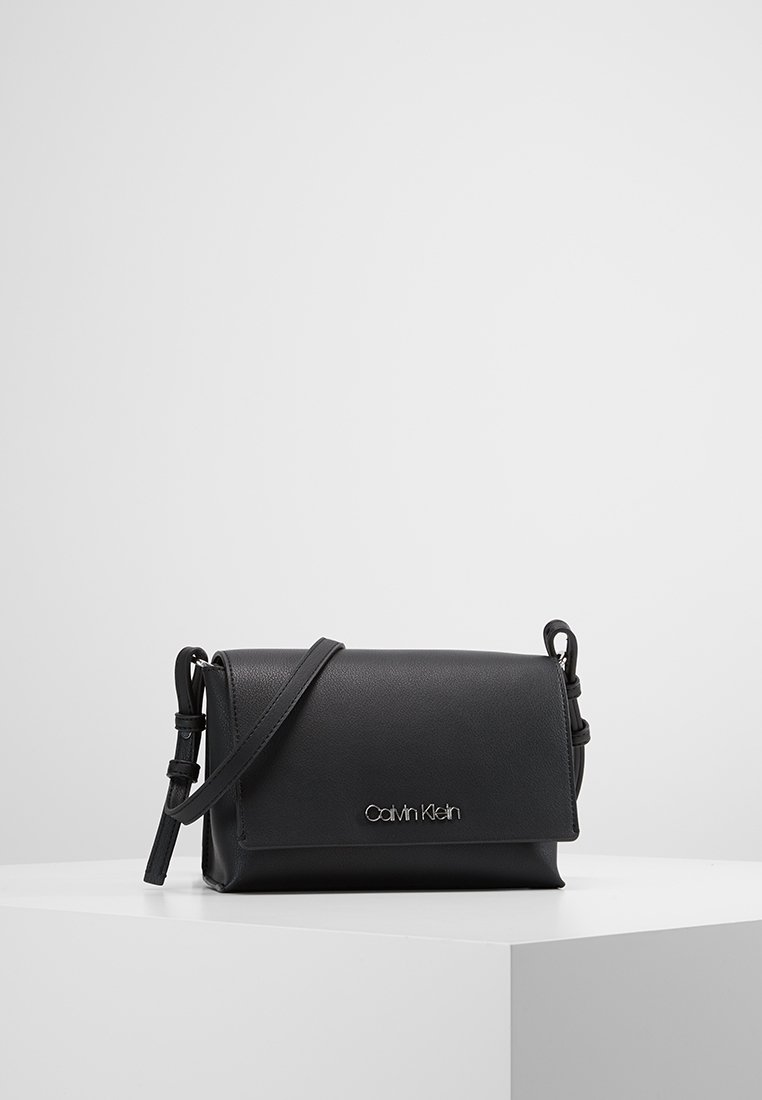 Černá kožená crossbody taška s designem klapky, stříbrným logem, nastavitelným popruhem, hladkým povrchem a obdélníkovým tvarem.