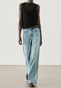 Débardeur en dentelle noire avec un col rond, associé à un jean large bleu clair. Des sandales complètent le look, mettant en avant une coupe décontractée.