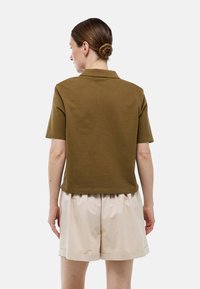 Polo à manches courtes en vert olive avec une texture lisse, comportant un col classique et une coupe décontractée, associé à un short beige clair.