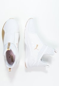 Białe sportowe buty slip-on Puma z złotymi akcentami, teksturowana cholewka i pętelki do zakładania, pokazane z widoku z góry i z boku na białym tle.