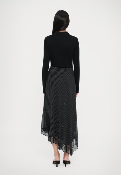 Top negro de manga larga con cuello, combinado con una falda a rayas en blanco y negro que presenta un acabado de encaje y un dobladillo asimétrico.