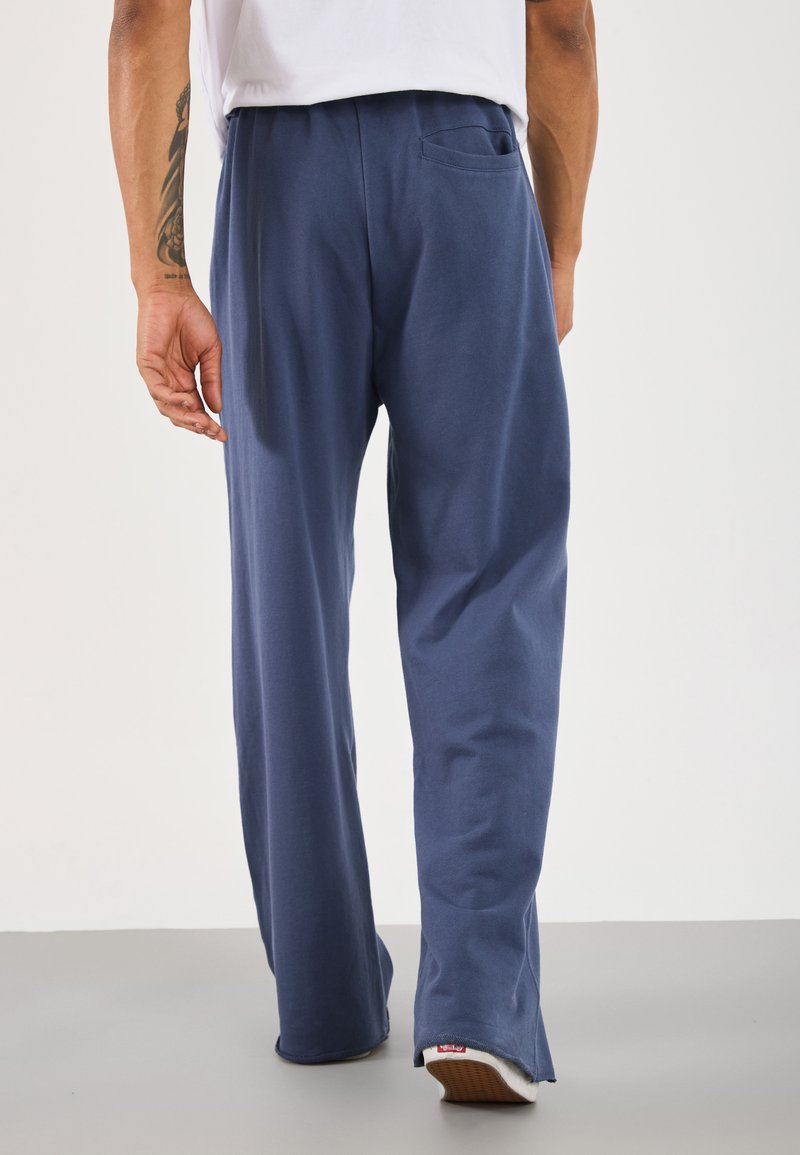 Pantaloni tuta in cotone blu con vestibilità comoda e tasca laterale. Presentano una consistenza morbida e orlo con leggere fessure alle caviglie.