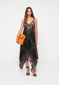 Vestido longo preto com decote em V, padrões florais e barra assimétrica. Combinado com uma bolsa laranja e sapatos de salto pretos com tiras.