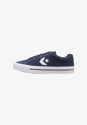 Zapatillas de lona azul marino con acentos blancos, que presentan un logo de estrella y una suela de goma texturizada, diseñadas con un perfil bajo y cierre de cordones.