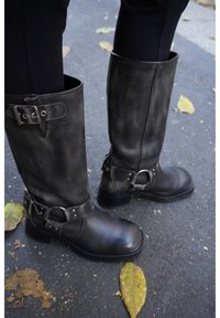 Black leather knee-high boots with metal buckles and accents, round toe, flat heel, and smooth texture, photographed outdoors.