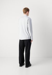 Lys grå langermet skjorte med en myk tekstur, kombinert med løse svarte bukser og svart fottøy. Enkelt design uten synlige mønstre.