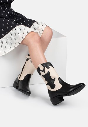 Bottines en cuir noir et beige avec un design découpé ondulé, un talon bas et une texture lisse. Convient pour une tenue décontractée.