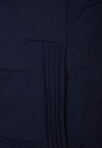 Granatowa kurtka puchowa o gładkiej fakturze, pikowanym wzorze i poziomych przeszyciach. Wzmocnione szwy zwiększają trwałość.