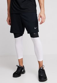 Black sports shorts with a gray Nike logo, layered over white compression leggings. Black athletic shoes complete the outfit.