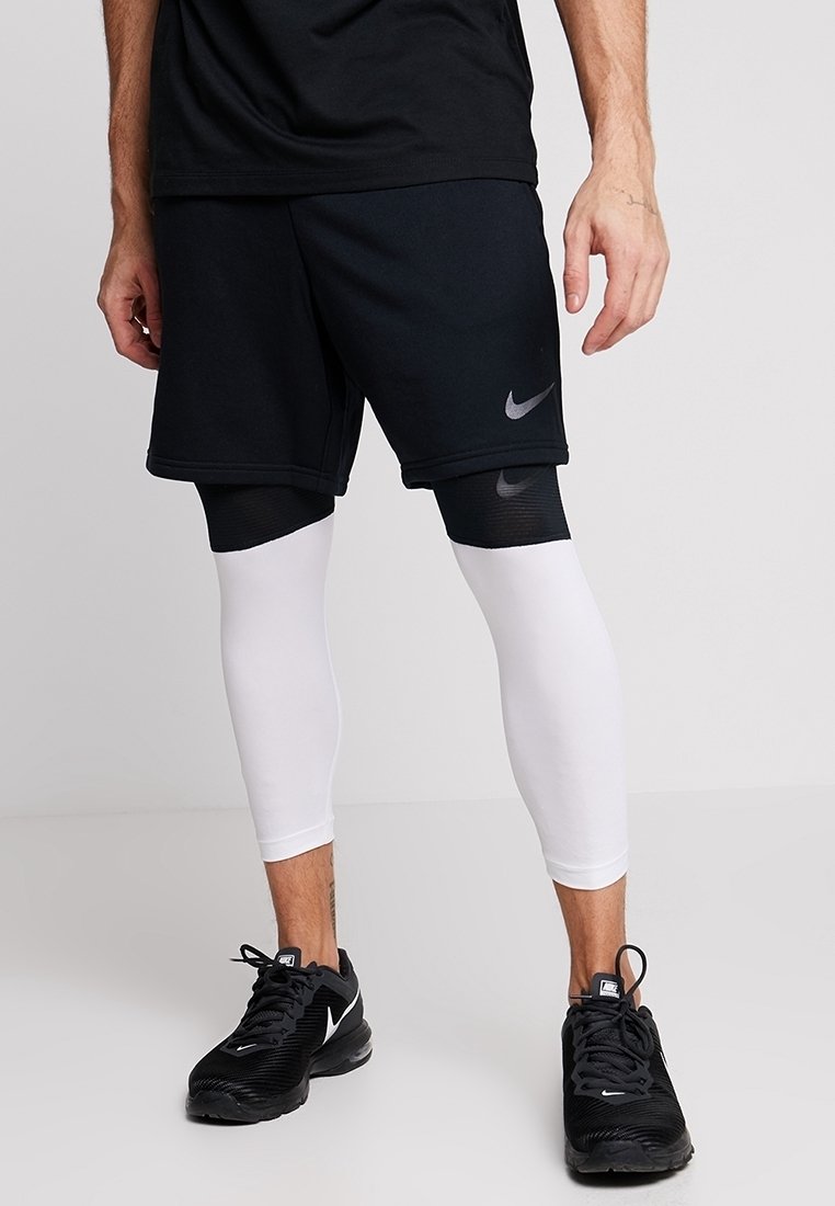 Black sports shorts with a gray Nike logo, layered over white compression leggings. Black athletic shoes complete the outfit.