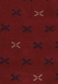 Czerwony materiał o teksturowanej powierzchni zdobiony jest wzorem małych kształtów 'X' w granatowym i beżowym kolorze, równomiernie rozmieszczonych na całej powierzchni.