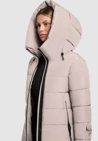 Lysebeige polstret jakke med høj krave og oversize hætte. Har sorte lynlåse og en sidelomme, samt en quiltet tekstur.
