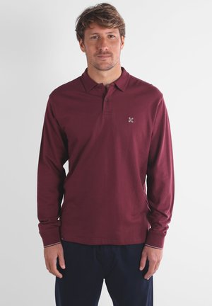 Polo à manches longues bordeaux avec col, présentant un petit logo sur la poitrine et des coutures contrastées aux poignets et à l'ourlet.