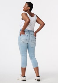 Jeans capri en denim bleu clair avec une taille élastique, dotés de deux poches arrière, de coutures plates et d'un design ajusté.