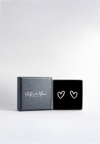 Silverhjärtformade örhängen i en svart sammetsfodrad ask, med en texturerad svart ytterdel och en vit logotyp på locket.