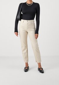 Svart långärmad topp, beige hög midja byxor med rak passform och svarta platta skor. Accessoarer inkluderar en svart väska och silverkedja halsband.