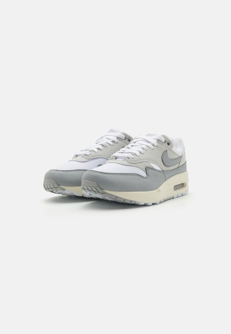 Grijze en witte sport sneakers met een bovenwerk van leer en mesh, een ronde neus, veters en zichtbare luchtkussens in de zool.