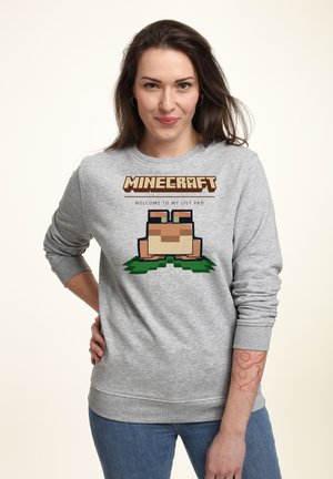 Szara bluza z kapturem z logo "Minecraft" i napisem "WITAJ NA MOIM LILIOWYM PODKŁADZIE", z pikselową grafiką żaby na zielonej trawie. Miękka faktura materiału.