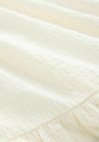 Materiał w kolorze kremowym o fakturowanym, tkanym wzorze, charakteryzujący się lekkim, miękkim materiałem i lekko pomarszczonym wyglądem.