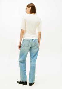 Biały, prążkowany, dopasowany top z krótkimi rękawami, zestawiony z jasnoniebieskimi prostymi jeansami, dopełniony czarnymi loafersami. Prosty, czysty design.