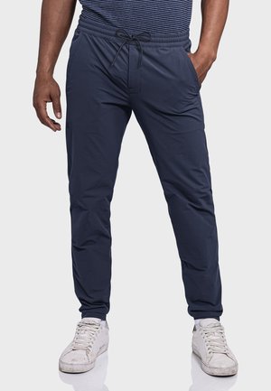 Navyblaue Jogginghosen mit elastischem Bund, Detail mit Kordelzug, seitlichen Taschen, schmaler Passform und glatter Textur, kombiniert mit weißen Sneakern.
