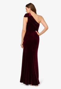 Abito in velluto bordeaux con design a spalla unica, silhouette aderente, taglio lungo fino al pavimento e dettagli di drappeggio delicati sulla spalla.